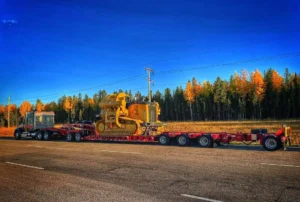 Heavy-duty yellow loader transported by Bowline Logistics across the Alberta border during a winter sunrise, with 'Oversize Load' signage