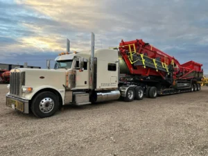 Bowline Logistics white Peterbilt semi-truck delivering red industrial screening equipment on a multi-axle trailer at a construction yard
