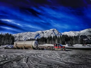Bowline Logistics truck hauls a galvanized metal structure for an energy facility under a bright blue sky