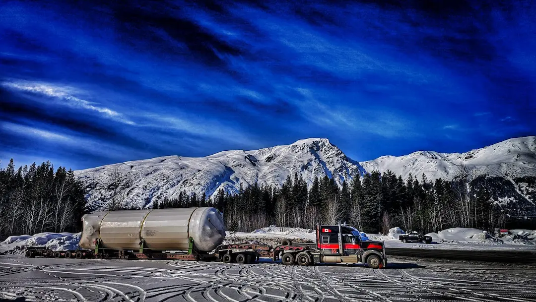 Bowline Logistics truck hauls a galvanized metal structure for an energy facility under a bright blue sky Bowline Logistics truck hauls a galvanized metal structure for an energy facility under a bright blue sky