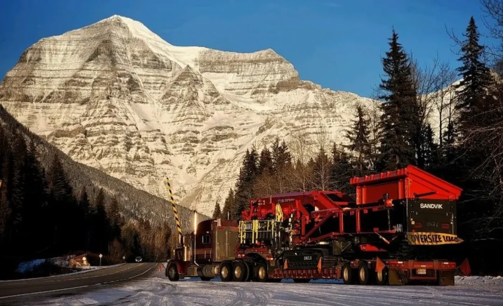Specialized Equipment Transport Trailer Bowline Logistics truck transporting red industrial equipment through a snowy mountain pass with oversized load signage